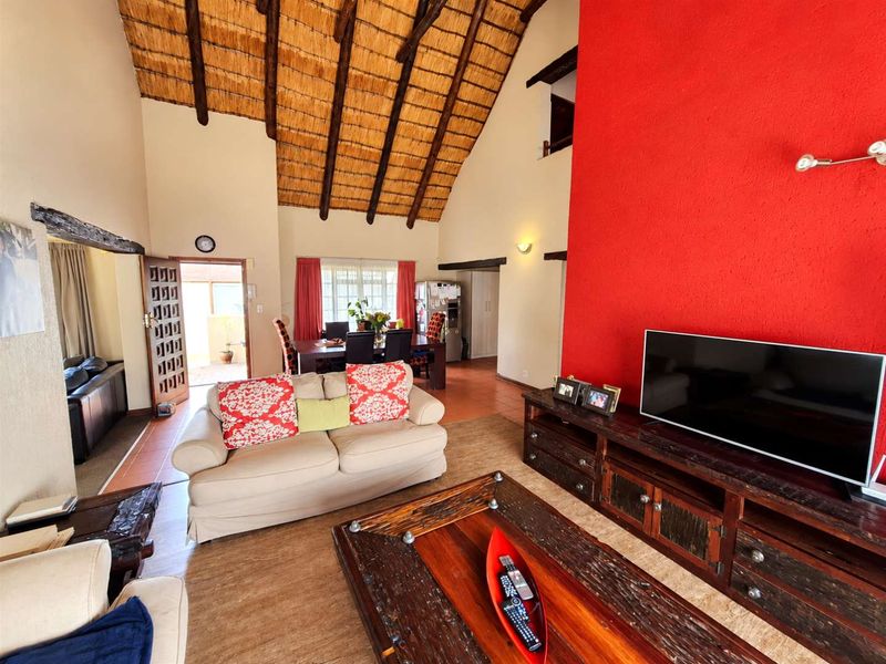 Spacious open-plan living and dining area featuring a high vaulted thatched ceiling with exposed timber rafters and a bold red feature wall.