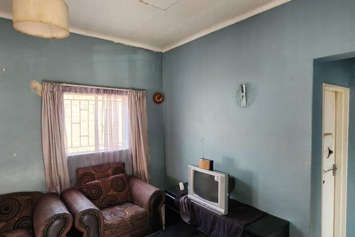 A living room area featuring security bars on the window, requiring cosmetic updates to the walls and ceiling to improve the overall condition.