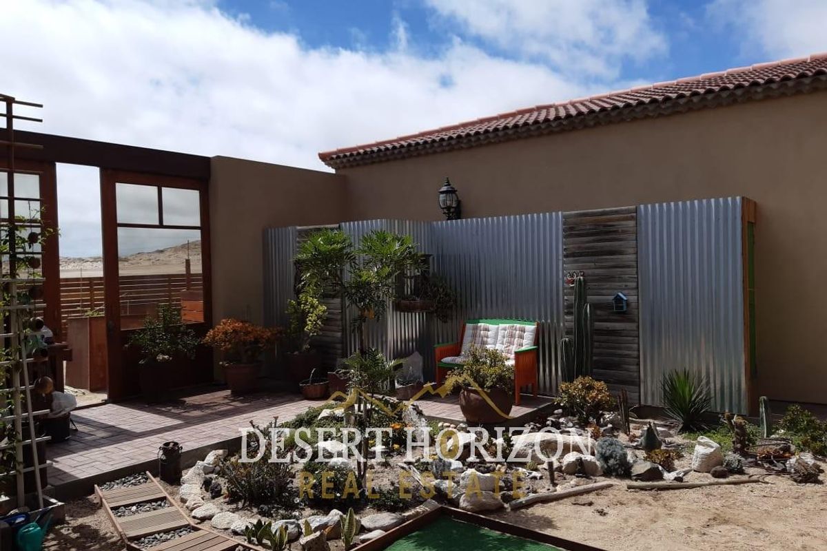 A private rear courtyard featuring a paved patio area, corrugated metal feature wall, and landscaped garden beds with desert-style planting.