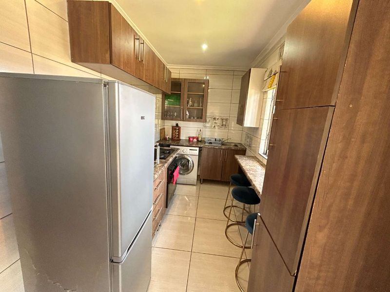 A functional galley-style kitchen featuring wood-finish cabinetry, tiled surfaces, integrated appliances, and a breakfast bar area.