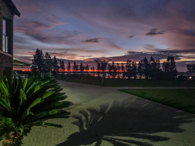 A scenic twilight view of the property grounds featuring a paved driveway and landscaped garden under a dramatic sunset sky.