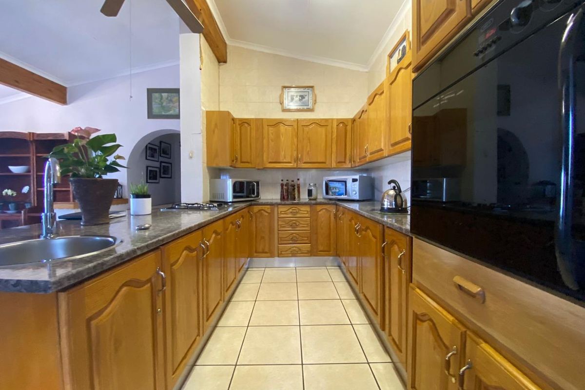 A functional kitchen featuring traditional timber cabinetry, granite-look countertops, tiled flooring, and integrated oven and hob appliances.