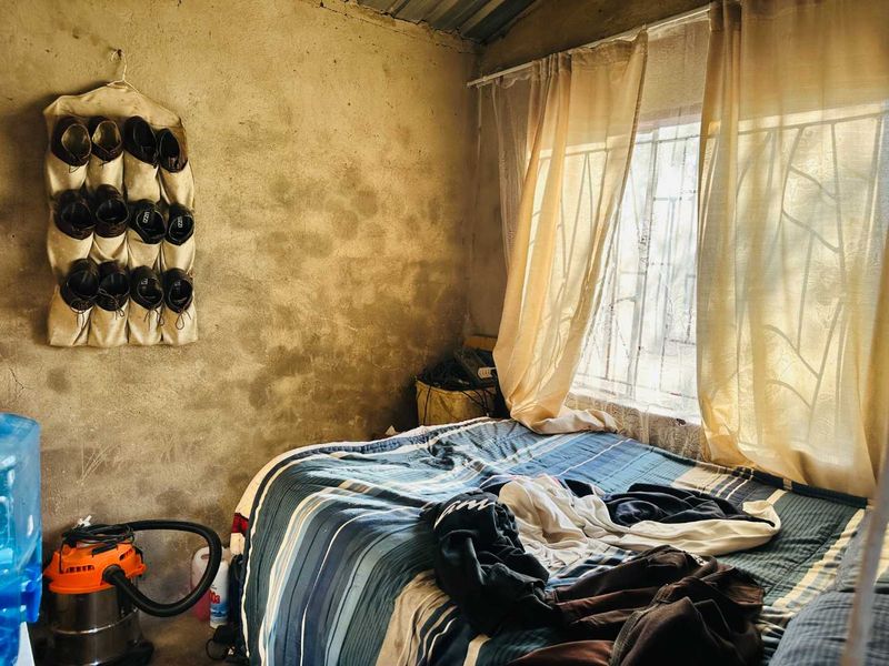 A bedroom featuring unfinished concrete walls and a window with security bars, requiring cosmetic updates to improve the overall finish and aesthetic appeal.