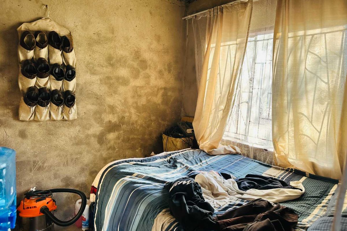 A bedroom featuring unfinished concrete walls and a window with security bars, requiring cosmetic updates to improve the overall finish and aesthetic appeal.