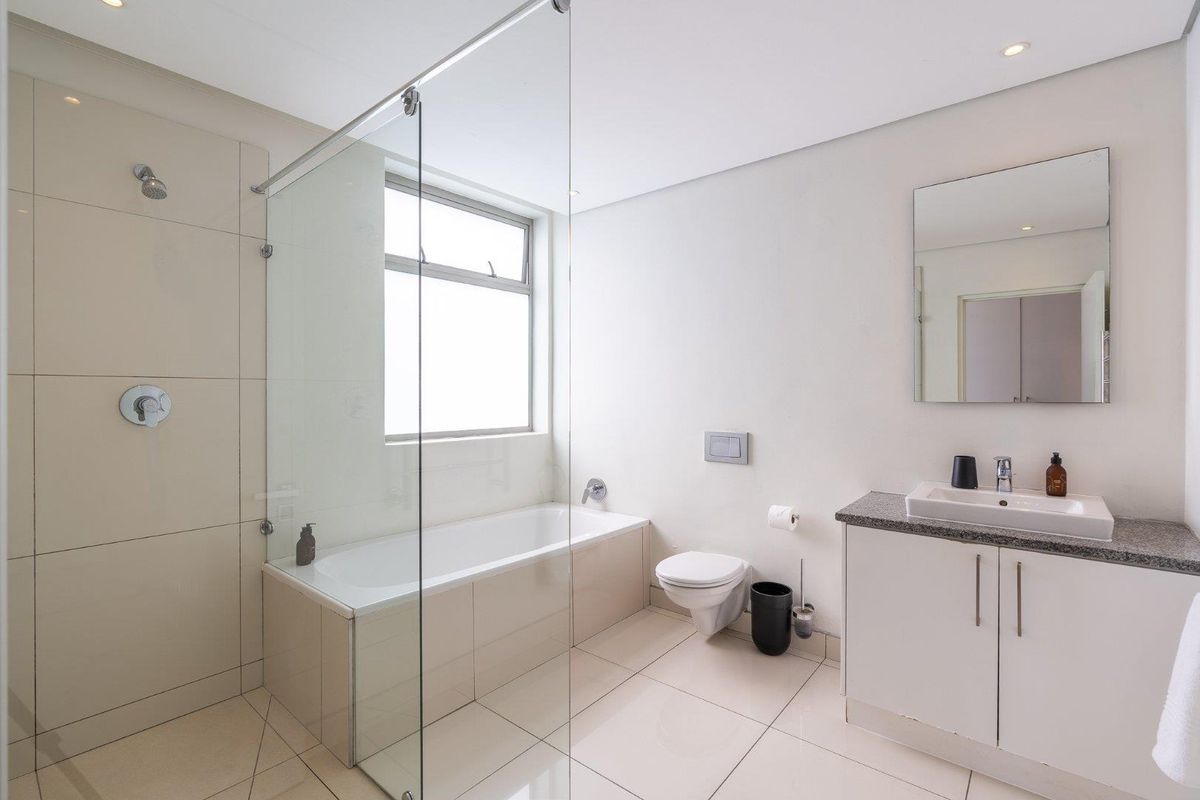 Modern bathroom featuring a glass-enclosed shower over a bathtub, wall-mounted toilet, and a vanity cabinet with a granite countertop.
