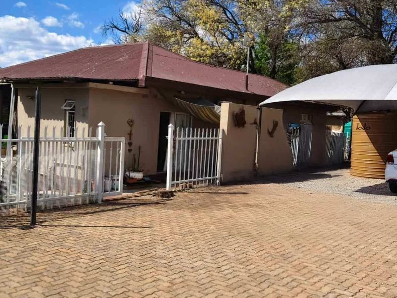 Front view of the property featuring a paved driveway, metal security fencing, a carport, and a water storage tank.