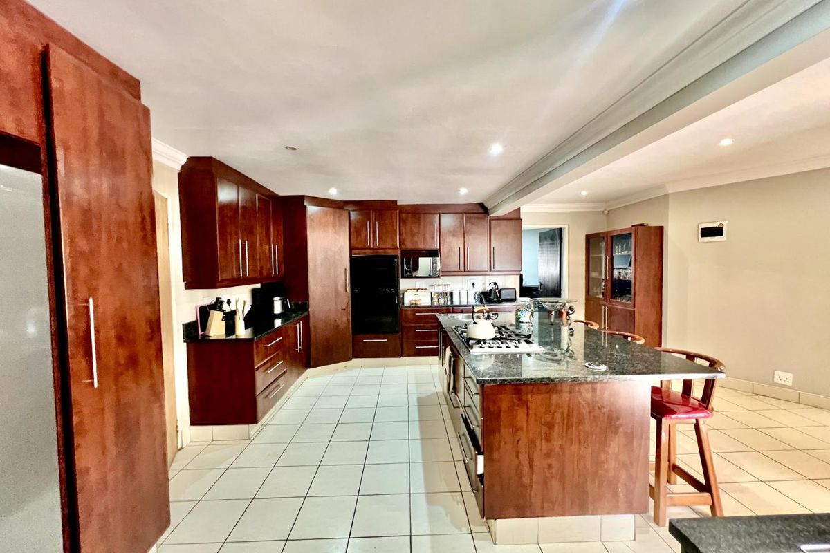 Spacious kitchen featuring dark wood cabinetry, granite countertops, a large central island with a gas hob, and tiled flooring throughout.