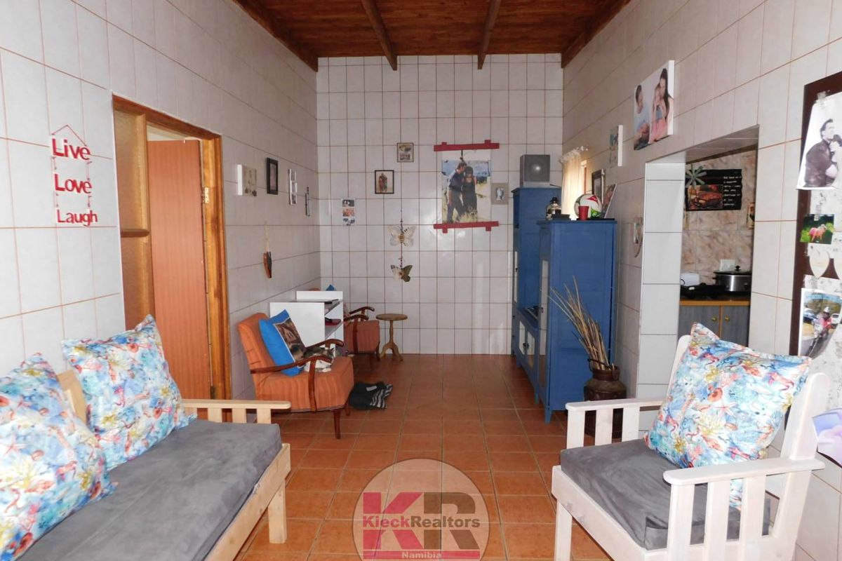 Living area featuring full-height wall tiling, exposed timber beam ceiling, and ceramic floor tiles, offering a functional space with potential for modernization.