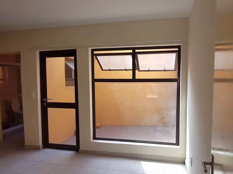 An empty living area featuring neutral tiled flooring and dark aluminium window and door frames, providing access to an exterior space.