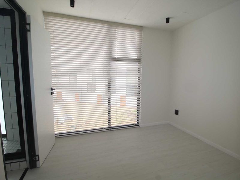 A bright, modern, and empty bedroom featuring neutral laminate flooring, recessed ceiling lighting, and fitted venetian blinds, offering a clean canvas for personalization.
