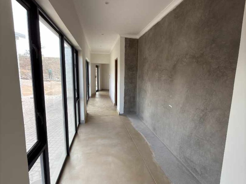 A long, modern hallway featuring polished concrete floors, large glass sliding doors, and an unfinished cement feature wall, offering a blank canvas for interior design.