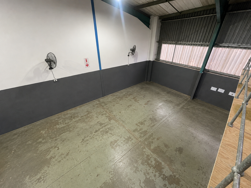 An empty industrial utility space featuring concrete flooring, wall-mounted fans, and corrugated metal wall cladding, suitable for storage or workshop use.