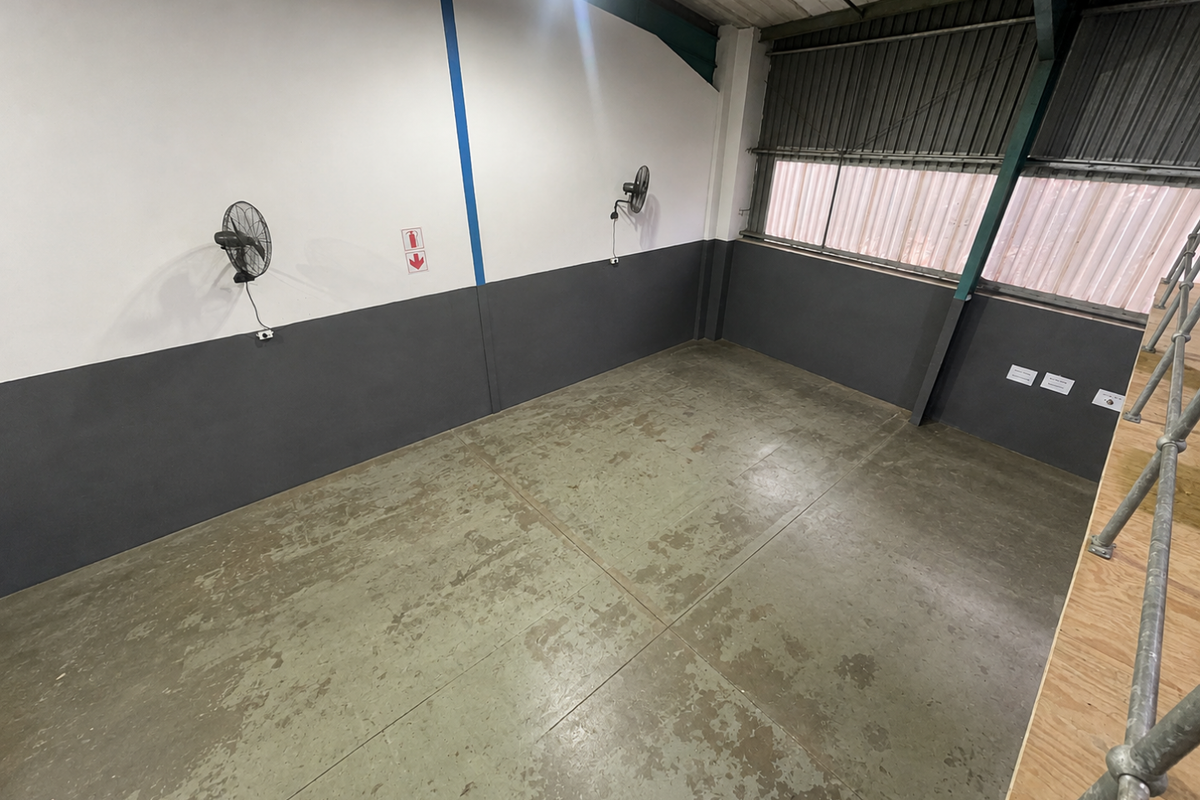 An empty industrial utility space featuring concrete flooring, wall-mounted fans, and corrugated metal wall cladding, suitable for storage or workshop use.