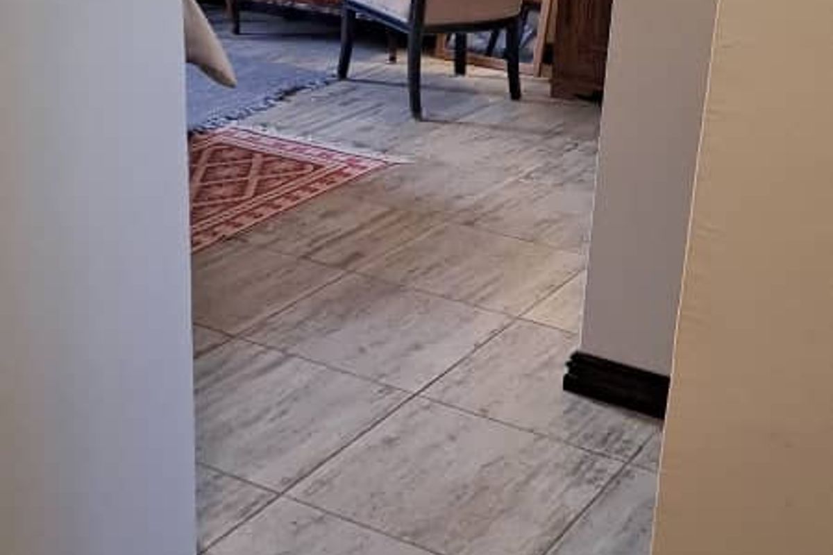 A view from a hallway into a living area featuring neutral tiled flooring and dark skirting boards.