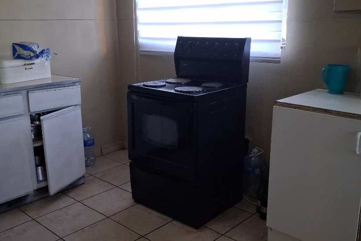 A functional kitchen area featuring tiled flooring, a freestanding electric stove, and basic cabinetry with visible wear.