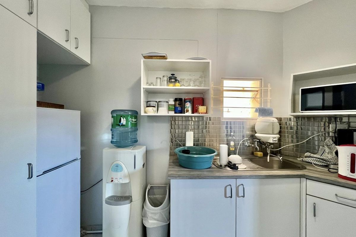 A compact office kitchenette featuring white cabinetry, a stainless steel sink, tiled backsplash, and built-in shelving for convenient staff use.