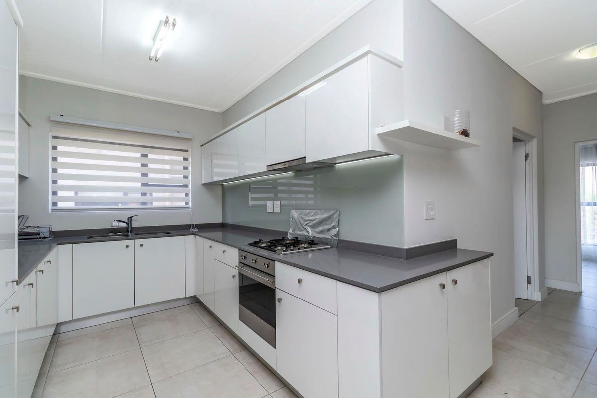 Modern kitchen featuring white high-gloss cabinetry, grey stone countertops, integrated gas hob, oven, and a glass splashback.