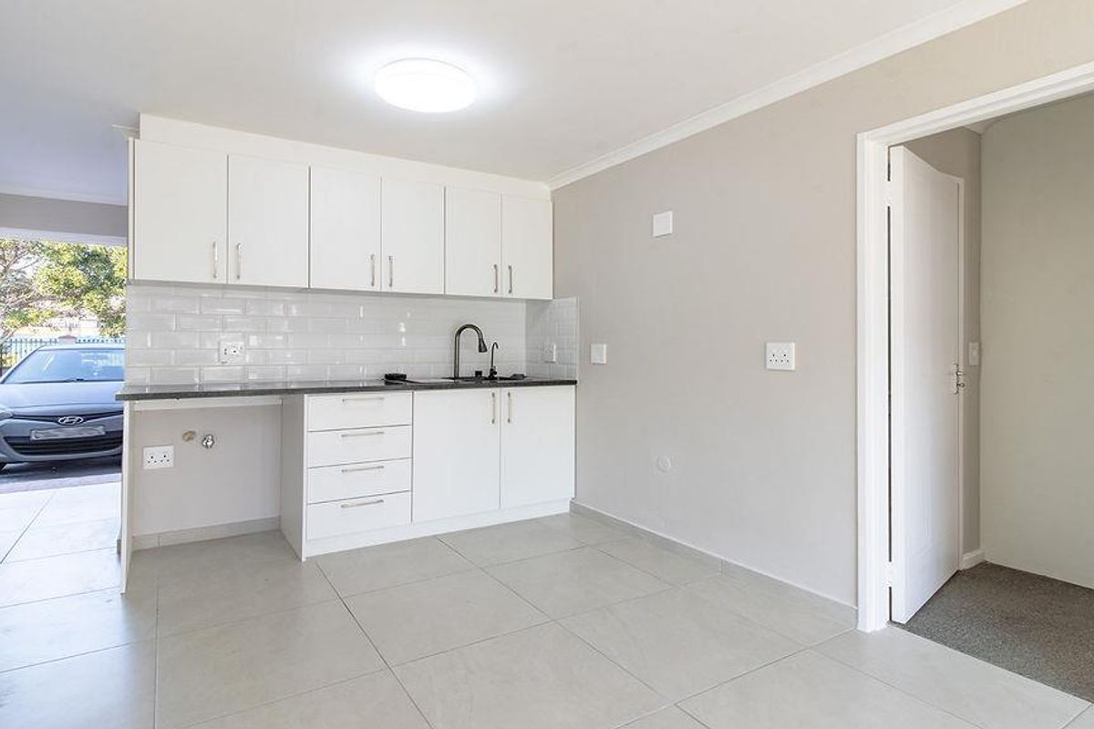 A clean, modern kitchen featuring white cabinetry, subway tile backsplash, and tiled flooring, with direct access to the exterior.
