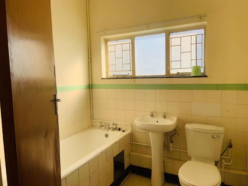A functional bathroom featuring a pedestal basin, bathtub, and toilet, with original tiled finishes and security bars on the window.