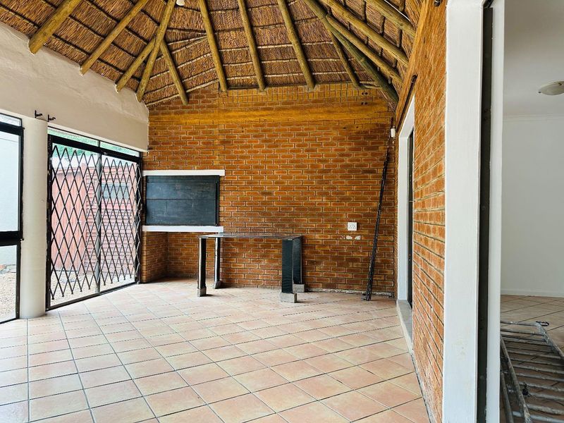 Covered patio area featuring a traditional thatched roof, exposed brick walls, tiled flooring, and a built-in braai facility.