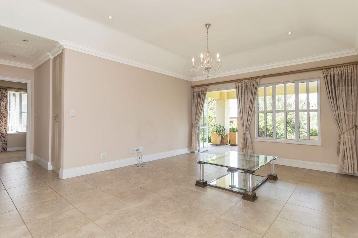 Spacious living area featuring neutral tiled flooring, decorative crown molding, a classic chandelier, and direct access to an outdoor patio through glass doors.