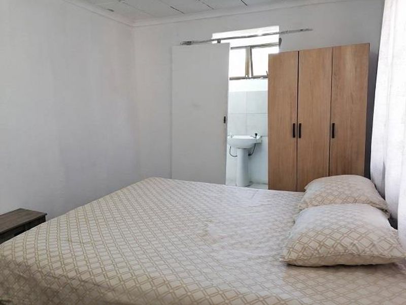 A bedroom featuring a built-in wardrobe and an en-suite pedestal basin, with visible wear to the ceiling finishes.