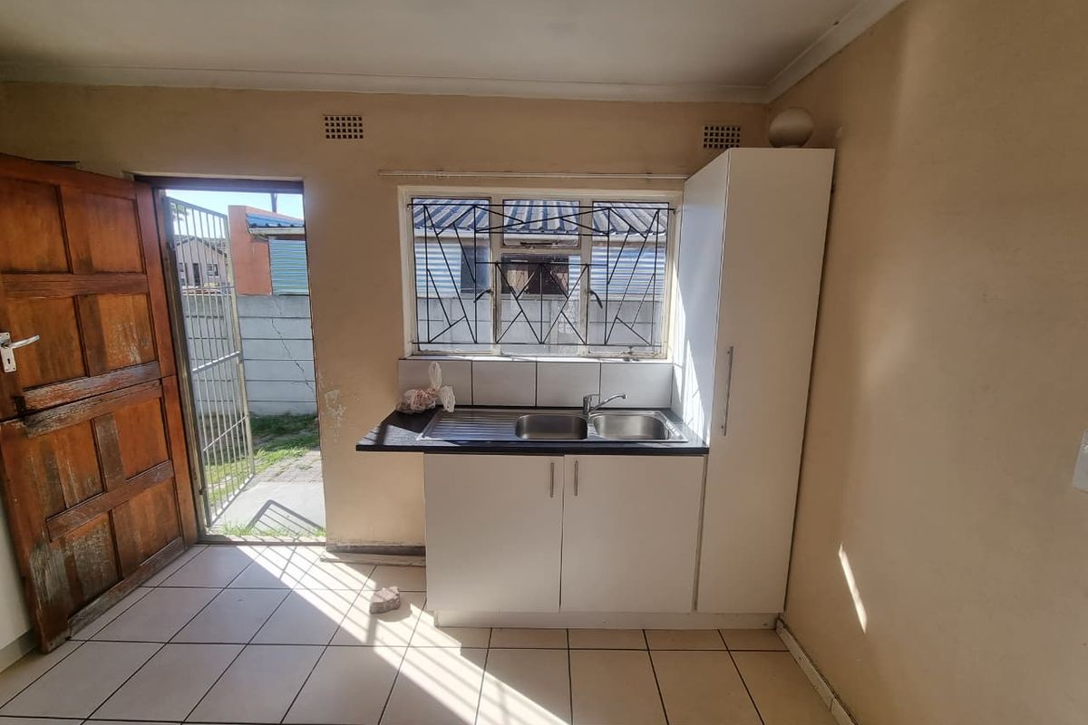 A compact kitchen area featuring a stainless steel sink, built-in cabinetry, tiled flooring, and direct access to the exterior through a wooden door.
