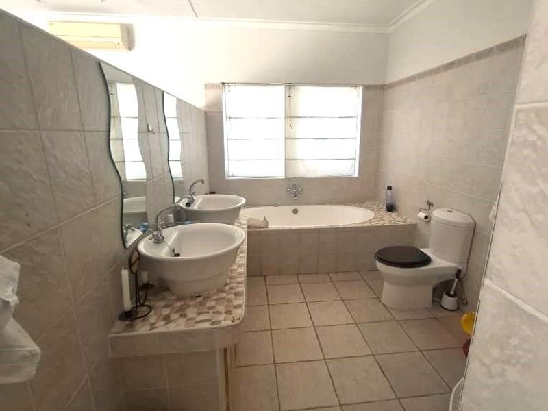 A functional bathroom featuring a dual vanity, built-in bathtub, toilet, and tiled finishes throughout, offering a practical layout with potential for modern updates.