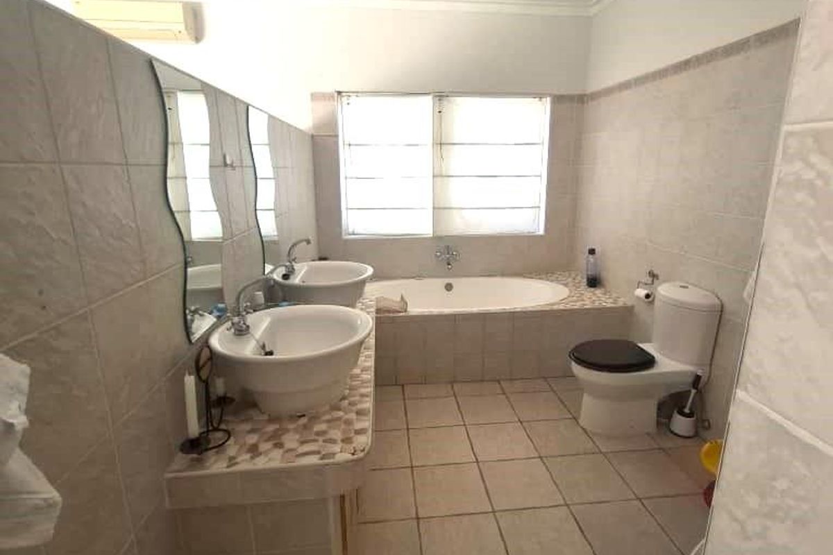 A functional bathroom featuring a dual vanity, built-in bathtub, toilet, and tiled finishes throughout, offering a practical layout with potential for modern updates.