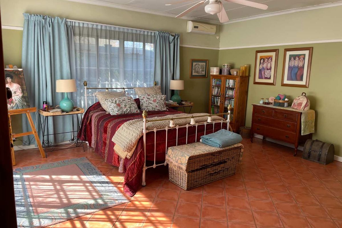 Spacious bedroom featuring terracotta floor tiles, a ceiling fan, and a wall-mounted air conditioning unit.