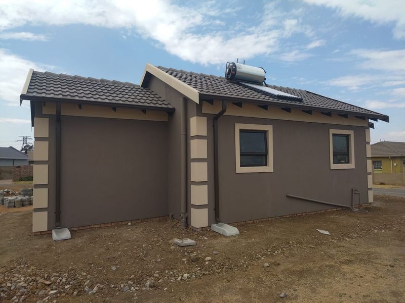 Rear view of a modern house featuring a tiled roof, solar water heating system, and finished exterior walls with aluminium window frames.