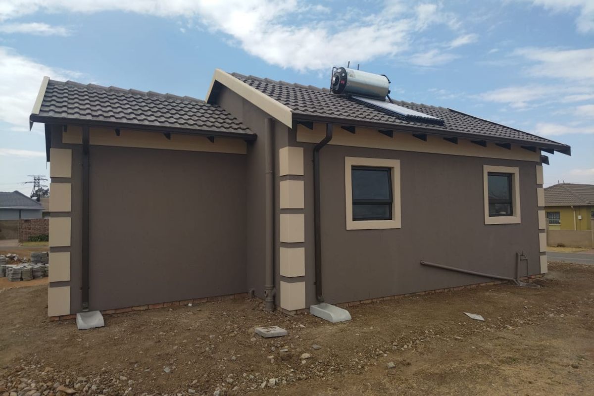 Rear view of a modern house featuring a tiled roof, solar water heating system, and finished exterior walls with aluminium window frames.