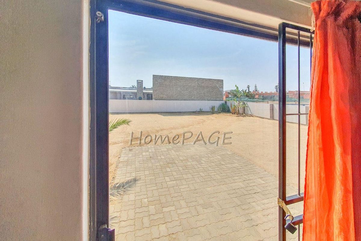 View from an interior doorway looking out onto a paved patio area and a large, open backyard with perimeter boundary walls.
