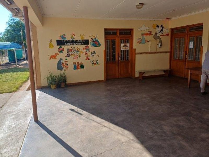 A covered outdoor patio area featuring concrete flooring, timber-framed glass doors, and a support pillar, suitable for an outdoor entertainment or play space.