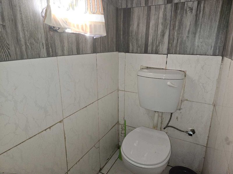 A small bathroom featuring a standard toilet with tiled walls and flooring, currently showing signs of wear and requiring maintenance.
