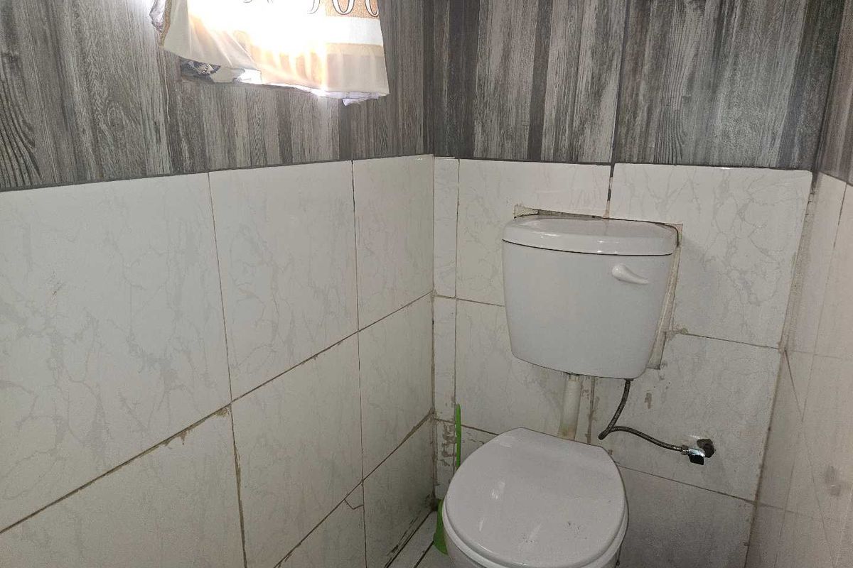 A small bathroom featuring a standard toilet with tiled walls and flooring, currently showing signs of wear and requiring maintenance.