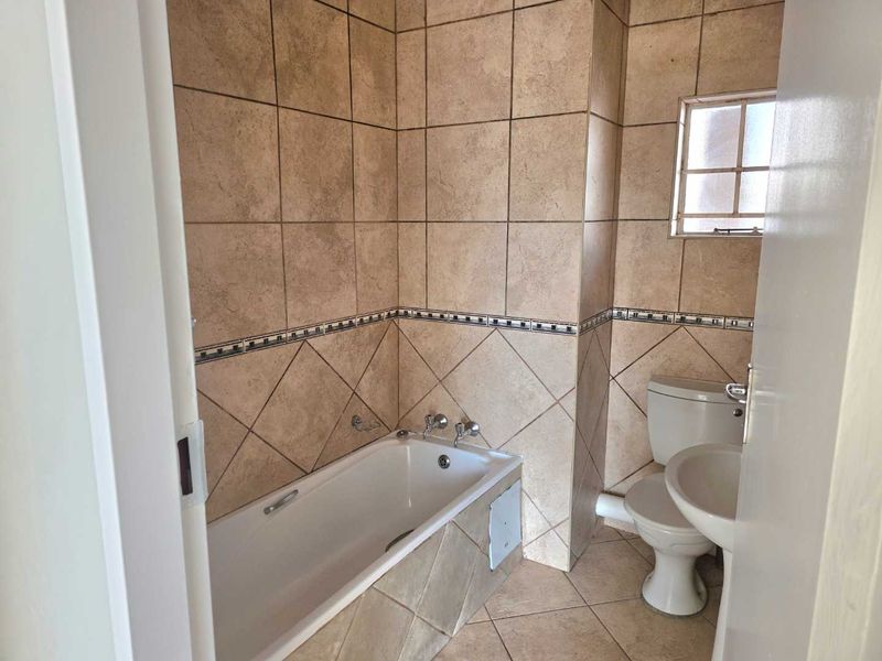 A functional bathroom featuring a bathtub, pedestal basin, and toilet, finished with neutral ceramic wall and floor tiles.
