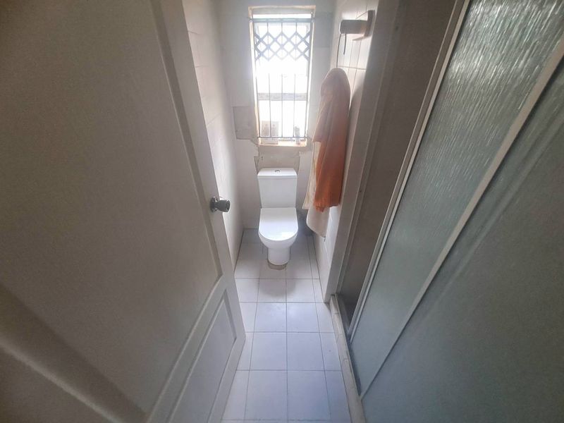A compact bathroom featuring a toilet, shower enclosure, and tiled finishes, currently requiring maintenance and cosmetic updates to the wall surfaces.