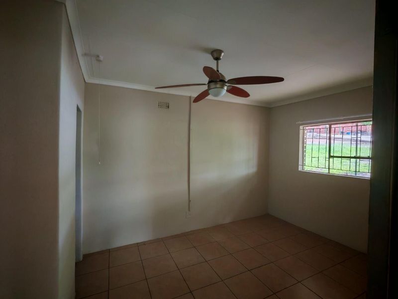 An empty bedroom featuring tiled flooring, a ceiling fan, and a window fitted with security bars.