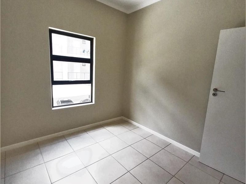 A clean, empty bedroom featuring neutral wall paint, tiled flooring, and a modern aluminium window frame, providing a versatile space ready for personalization.