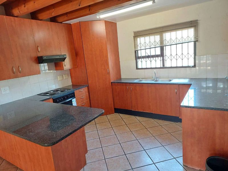 A functional kitchen featuring laminate cabinetry, granite countertops, built-in oven and hob, and exposed timber ceiling beams.
