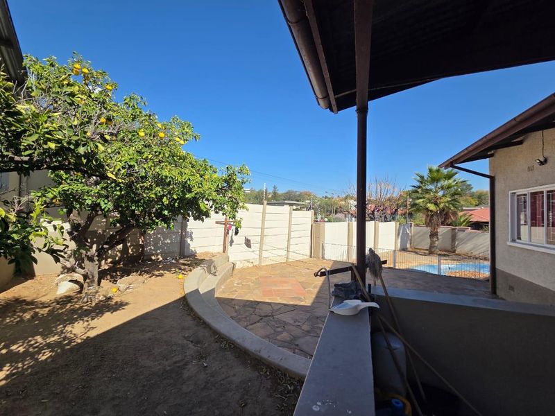 Rear garden area featuring a paved patio, covered veranda, and swimming pool, enclosed by a precast concrete boundary wall.