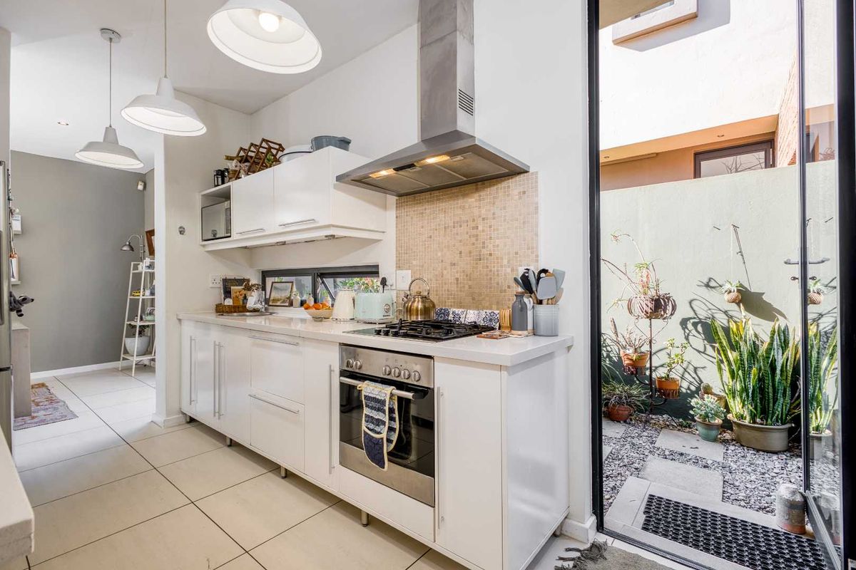 Modern kitchen featuring white cabinetry, stone countertops, gas hob, built-in oven, and a mosaic tile splashback, with direct access to a small outdoor courtyard.
