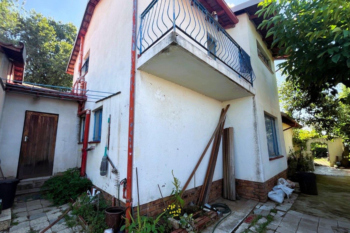 Rear exterior view of the house featuring a balcony with wrought iron railing, paved patio area, and visible wear on the exterior wall finishes.