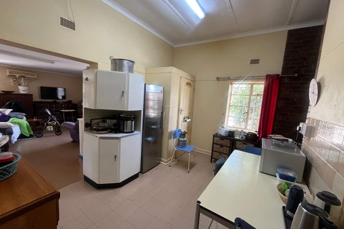 A dated kitchen area featuring original cabinetry, tiled flooring, and an exposed brick feature wall, offering potential for a modern renovation.