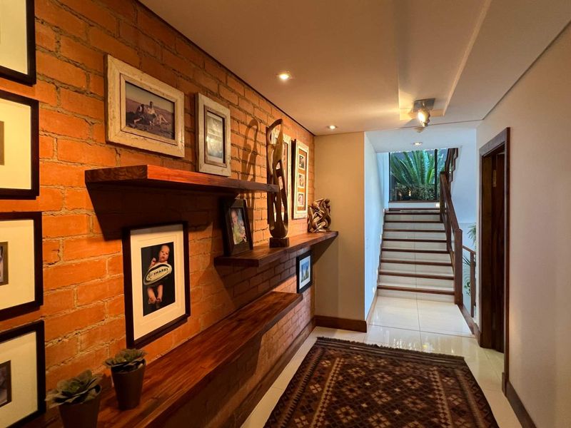 A well-lit hallway featuring an exposed brick feature wall with integrated timber shelving, leading to a staircase with a timber handrail.