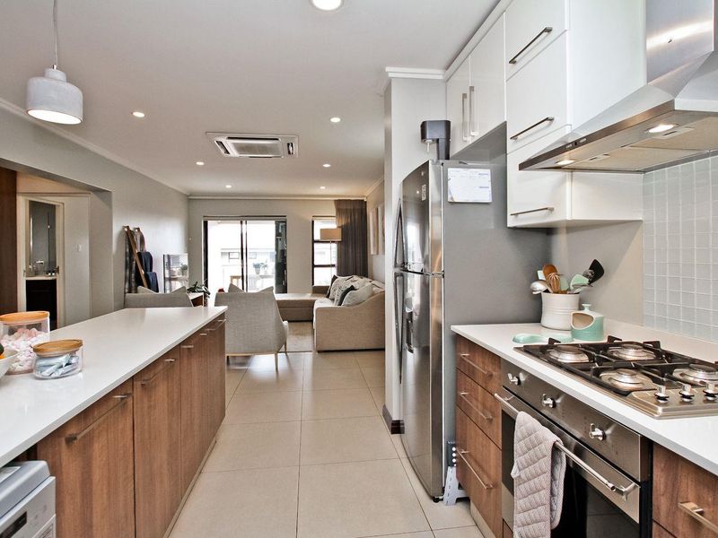 Modern open-plan kitchen and living area featuring stone countertops, gas hob, built-in cabinetry, and tiled flooring with integrated ducted air conditioning.