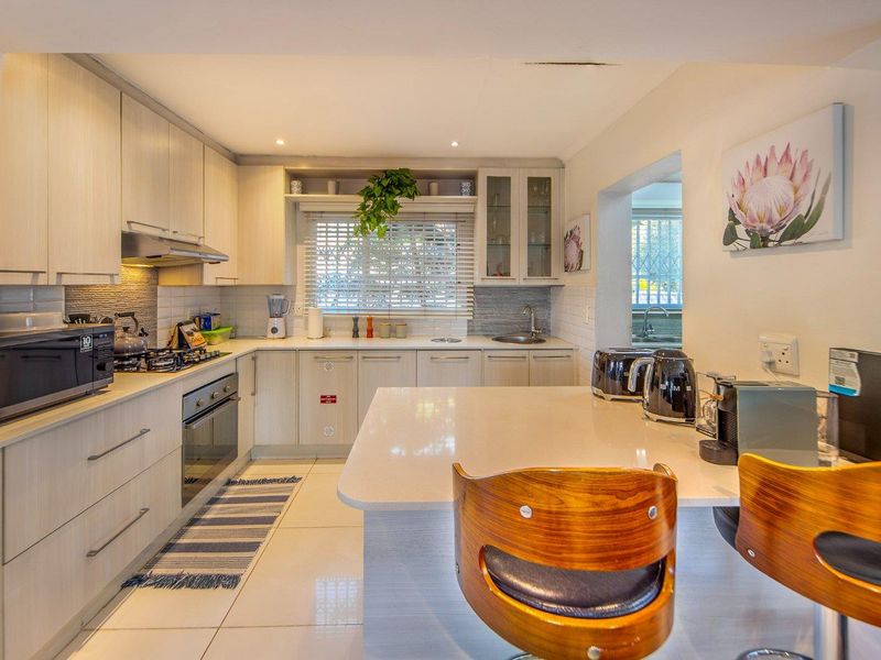 Modern kitchen featuring light wood cabinetry, stone countertops, a central island, and integrated appliances, offering a clean and functional cooking space.