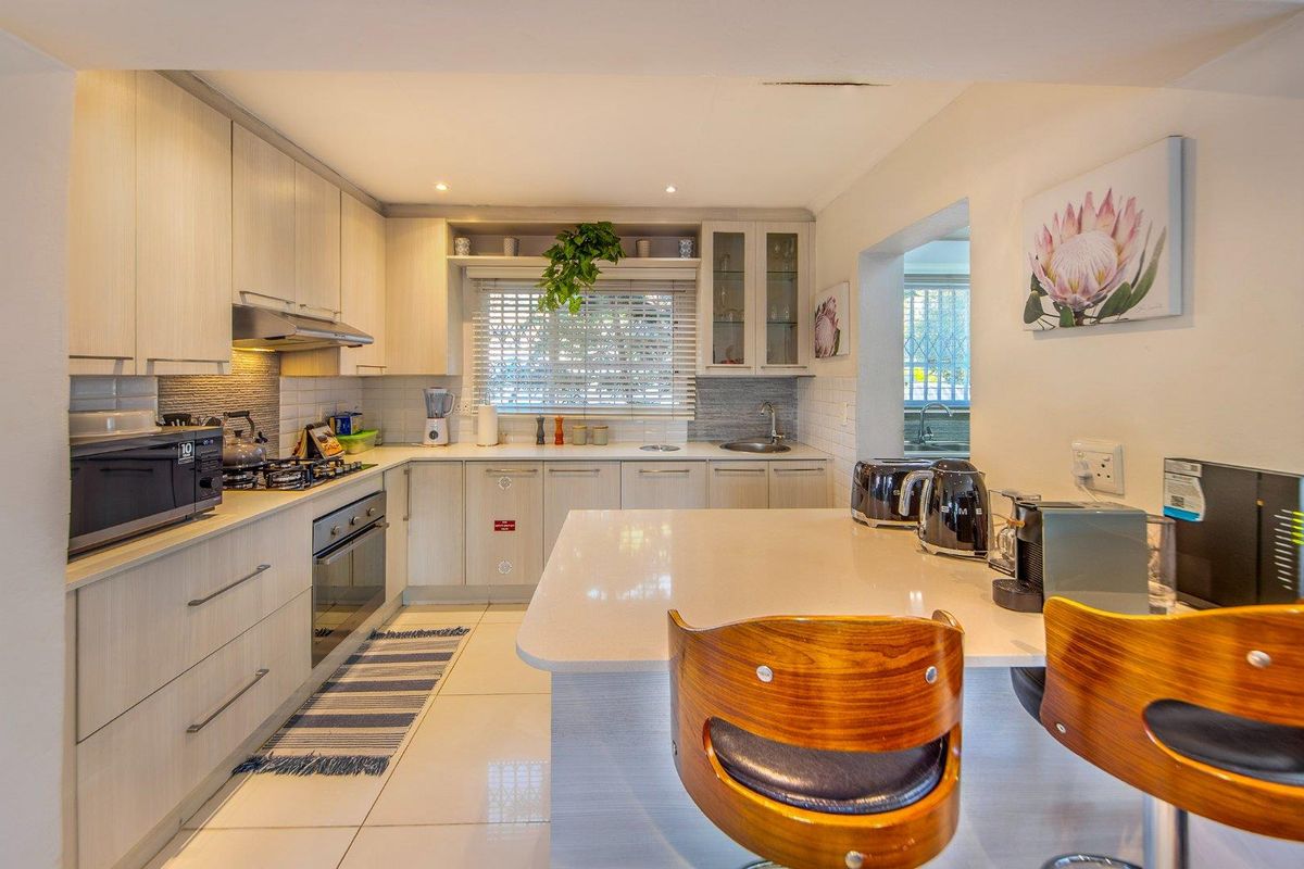Modern kitchen featuring light wood cabinetry, stone countertops, a central island, and integrated appliances, offering a clean and functional cooking space.