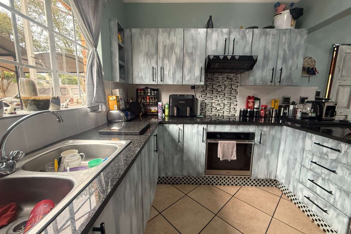 A functional kitchen featuring granite countertops, built-in oven, extractor fan, and double basin sink with tiled flooring and custom-painted cabinetry.